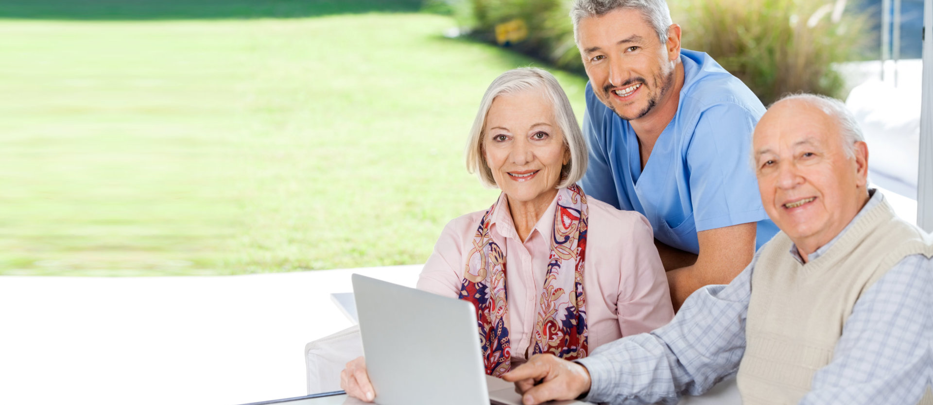 Portrait of smiling male caretaker and senior couple with laptop at nursing home porch